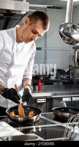 Chef professionnel cuisine des crevettes dans une poêle à frire avec de l'huile d'olive dans la cuisine du restaurant Banque D'Images