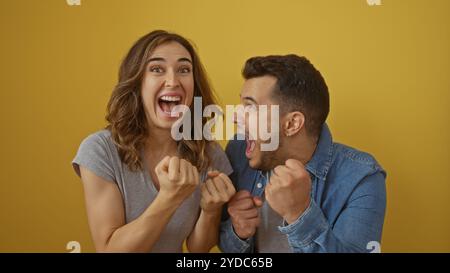 Homme et femme excités célébrant ensemble sur un fond jaune vibrant, mettant en valeur la joie, le bonheur et une relation énergique dans un s décontracté Banque D'Images