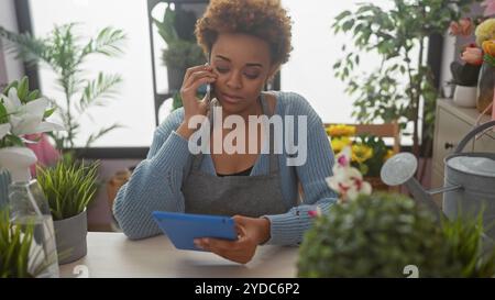 Une femme afro-américaine utilise un téléphone dans un magasin de fleurs intérieur entouré de plantes et de fleurs. Banque D'Images