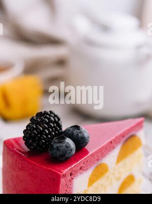 Une tranche de cheesecake rose à la fraise servie avec des baies fraîches sur un tableau blanc Banque D'Images