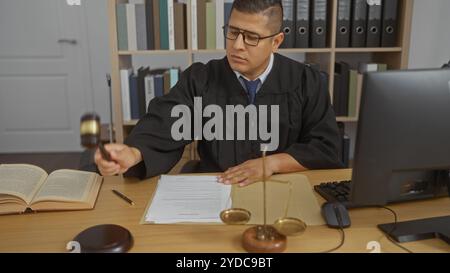 Jeune homme dans un espace de travail de bureau intérieur dépeignant un avocat ou un juge à l'aide d'un marteau et examinant des documents juridiques à son bureau Banque D'Images