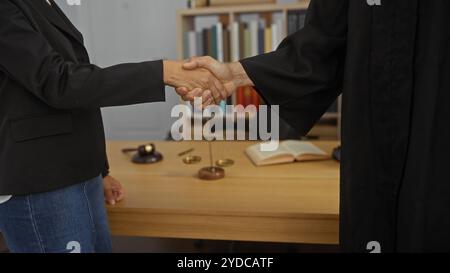 Homme et femme serrant la main dans le bureau d'un avocat avec des balances de justice et des livres juridiques sur le bureau Banque D'Images