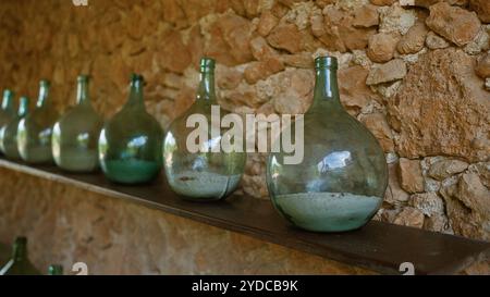 Des bouteilles en verre rustiques soigneusement disposées sur une étagère contre un mur de pierre texturée dans un cadre intérieur créent une atmosphère vintage et nostalgique. Banque D'Images