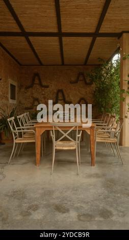 Patio extérieur avec une table en bois vide entourée de chaises sous un plafond rustique avec des plantes en pot améliorant l'ambiance terreuse dans un medite Banque D'Images