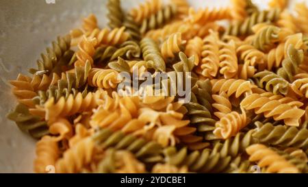 Gros plan de pâtes fusilli non cuites aux teintes vertes et oranges disposées en pile suggérant un thème culinaire italien Banque D'Images
