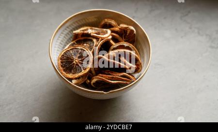 Bol de tranches de citron séchées sur une surface en béton gris à la lumière naturelle, soulignant la texture rustique et l'option collation saine. Banque D'Images