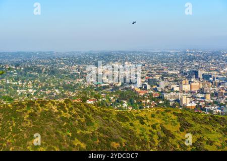 Los Angeles, Californie - 19 avril 2024 : vaste vue de Los Angeles mettant en valeur le développement urbain et la verdure, avec un hélicoptère volant au-dessus du Banque D'Images