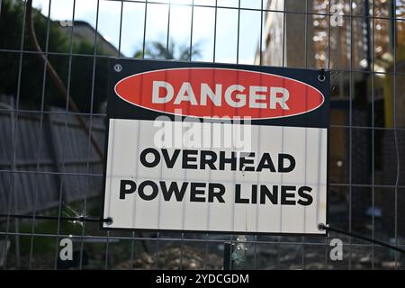 Panneau rectangulaire de lignes électriques aériennes de danger fixé à une clôture métallique basculante, à l'extérieur du chantier d'une maison de banlieue Banque D'Images