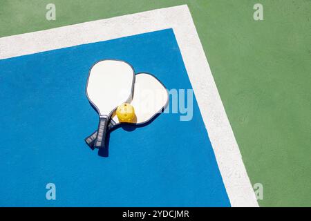 Deux pagaies de pickleball et une balle jaune reposent sur un terrain extérieur bleu et vert. Couleurs contrastées de l'aire de jeux et un jeu sportif énergique. Co Banque D'Images