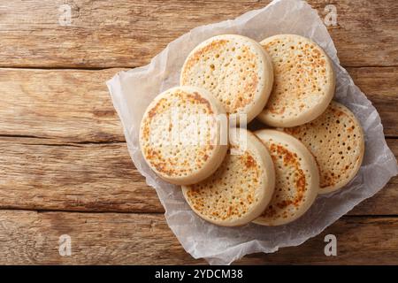 Fraîchement sortis du four des crumpets anglais ou du pain poreux gros plan sur du parchemin sur une vieille table. Vue horizontale de dessus Banque D'Images