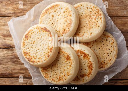 Gros plan poreux de crumpets anglais faits maison sur papier parchemin sur une vieille table. Vue horizontale de dessus Banque D'Images