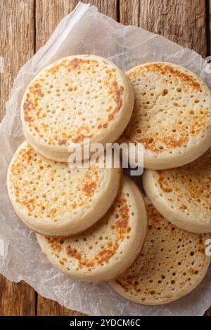 Freshly Baked Crumpet est une crêpe ronde faite de pâte poreuse gros plan sur un parchemin sur une table. Vue de dessus verticale Banque D'Images