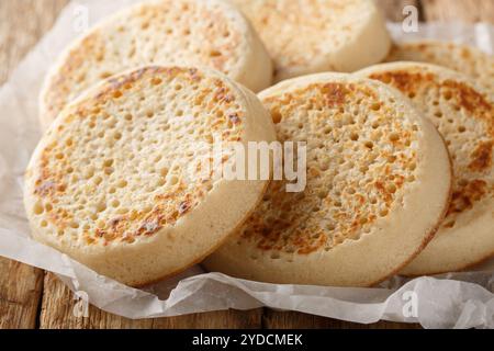 Fraîchement sortis du four des crumpets anglais ou du pain poreux gros plan sur du parchemin sur une vieille table. Horizontal Banque D'Images