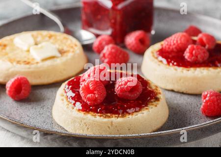 Petit déjeuner de crumpets britanniques avec beurre et confiture de framboises en gros plan sur l'assiette sur la table. Horizontal Banque D'Images