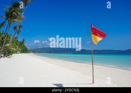 Drapeau de sécurité rouge et jaune sur une plage de sable blanc tropical avec de l'eau turquoise claire et des palmiers à Boracay, Philippines Banque D'Images
