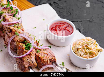 Kebabs juteux de porc sur des brochettes disposées sur une planche décorative Banque D'Images