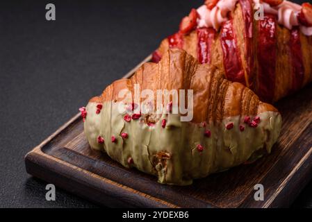 Croissant rouge sucré croustillant à la pistache, à la framboise et à la fraise sur un fond de béton foncé Banque D'Images