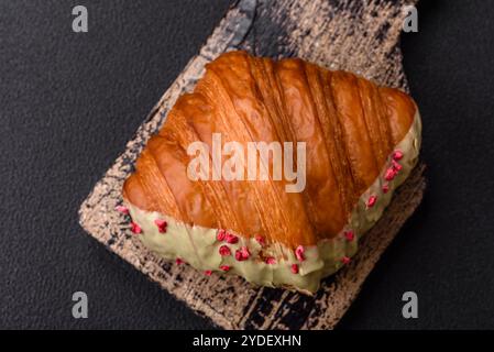 Croissant rouge sucré croustillant à la pistache, à la framboise et à la fraise sur un fond de béton foncé Banque D'Images