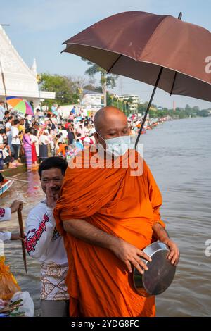 Un homme qui se tient derrière le chef moine Luang Por Chamnan est vu faire le salut traditionnel thaïlandais et le geste de respect, sur la rivière Chao Phraya au temple Wat Chin Wararam Worawihan, dans la province de Pathum Thani, en Thaïlande. La tradition de donner l'aumône à une centaine de moines à Pathum Thani, en Thaïlande, est une cérémonie bouddhiste vieille de plusieurs siècles qui se tient le long des rivières et des canaux après la fin du Carême bouddhiste. Les moines se rassemblent dans des bateaux pour recevoir des offrandes des habitants, qui préparent la nourriture et participent à la création de mérite. Cet événement célèbre la communauté, la foi et le patrimoine culturel. Banque D'Images