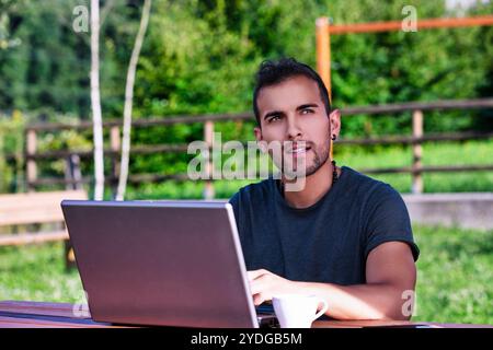 Jeune freelance travaille à distance dans un parc, profitant du café et de la nature, trouvant inspiration et équilibre dans un environnement serein Banque D'Images