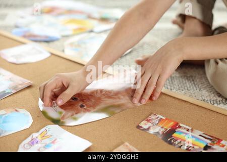 Petit garçon créant un tableau de vision avec différentes images et d'autres éléments sur le sol à l'intérieur, gros plan Banque D'Images