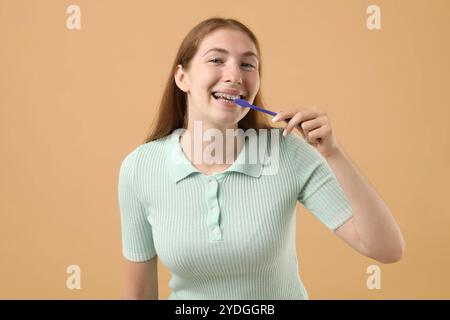 Fille avec des accolades nettoyant les dents sur fond beige Banque D'Images