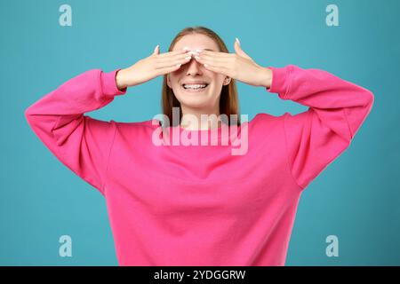 Fille souriante avec des bretelles couvrant les yeux sur fond bleu clair Banque D'Images