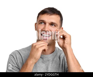 Homme avec des appareils dentaires nettoyant les dents à l'aide de fil dentaire sur fond blanc Banque D'Images