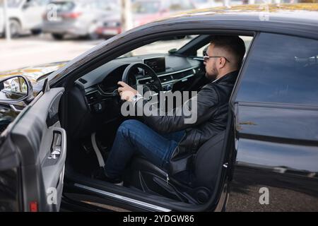 L'homme sort de la voiture. Bel homme barbu dans des lunettes de soleil assis dans la voiture Banque D'Images
