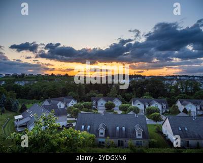 Un coucher de soleil orange vibrant illumine le ciel avec des teintes d'or et de rose, projetant une lueur chaude sur un quartier d'été paisible aux États-Unis, où clou Banque D'Images