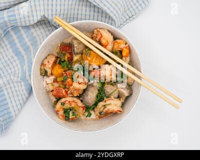 Une photo au-dessus d'un plat de fruits de mer de crevettes asiatiques servi dans un bol blanc, avec des baguettes posées à proximité. La configuration comprend une serviette bleue sur le côté, Banque D'Images