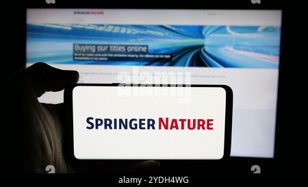 Personne tenant le téléphone portable avec le logo de la société d'édition académique Springer nature sur l'écran en face de la page Web d'affaires. Concentrez-vous sur l'affichage du téléphone. Banque D'Images