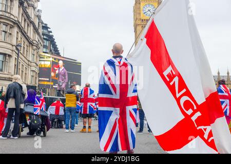 Londres, Royaume-Uni. 26 OCT, 2024. Un homme portant l'Union Jack agite le drapeau de la croix de Saint Georges alors que des milliers de personnes se rassemblaient pour le rassemblement Unite the Kingdom organisé par Tommy Robinson, qui n'était pas présent en raison de sa détention en prison, rassemblant à Victoria la marche s'est pacifiquement dirigée vers la place du Parlement où un nouveau documentaire « Lawfare » a été projeté. Stand Up to Racism a mobilisé une contre-protestation avec des milliers de personnes, qui se sont rassemblées pacifiquement à l'autre bout de whitehall. Crédit Milo Chandler/Alamy Live News Banque D'Images