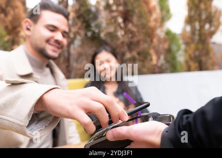 Jeune homme avec petite amie assis au café trottoir et payant sans contact Banque D'Images