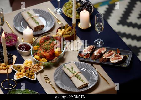Plan à grand angle de l'assiette à dîner avec serviette en lin décorée avec branche de romarin servi sur la table de fête avec poulet rôti et bougies allumées la veille de Noël, espace copie Banque D'Images