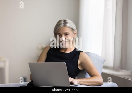 Belle vieille dame utilisant un ordinateur portable sur le canapé au salon Banque D'Images