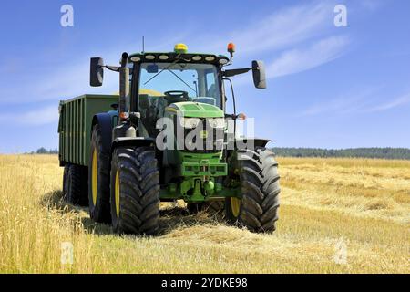 Tracteur agricole John Deere 6155R et remorque agricole Kire pleine de blé récolté dans le champ par une belle journée. Salo, Finlande. 25 juillet 2021 Banque D'Images