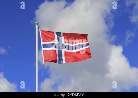 Drapeau de la Norvège contre le ciel bleu et les nuages blancs. Le drapeau de la Norvège est rouge avec une croix scandinave bleu indigo fimbriée en blanc Banque D'Images