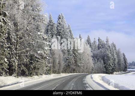 Arbres givrés et enneigés par la route principale vide en Finlande par une belle journée en hiver Banque D'Images