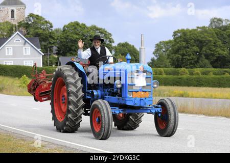 Kimito, Finlande. 6 juillet 2019. Homme en costume traditionnel salue alors qu'il conduit Fordson Super Major sur Kimito Tractorkavalkad, défilé de tracteurs vintage Banque D'Images