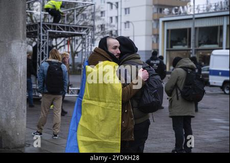 24.02.2023, Berlin, Allemagne, Europe, trois participants se tiennent fermement embrassés devant le Café Moskau, qui a été brièvement rebaptisé Café Kiev, devant o Banque D'Images