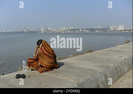 08.12.2011, Mumbai, Maharashtra, Inde, Asie, une femme est assise sur la promenade du front de mer le long de Marine Drive avec la ligne d'horizon de Malabar Hill à l'arrière Banque D'Images