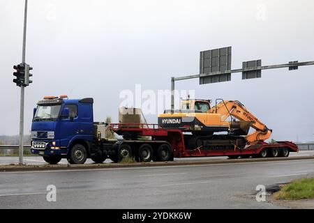 Camion bleu Volvo FH transportant l'excavatrice Hyundai Robex sur semi-remorque attend dans les feux de circulation le matin brumeux. Salo, Finlande. 24 septembre 2021 Banque D'Images