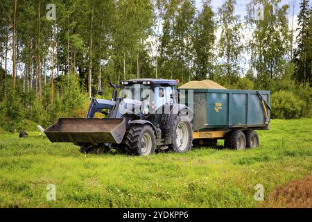 Tracteur agricole Valtra argenté avec remorque Multiva pour le grain récolté par champ, lors d'une journée de récolte d'automne claire. Koski Tl, Finlande. 11 septembre 20 Banque D'Images