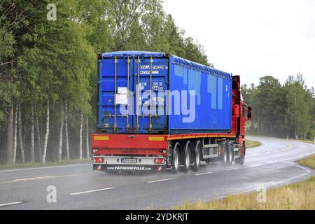 Red Truck transporte une remorque bleue de conteneur d'expédition le long de l'autoroute humide le jour de pluie. Vue arrière. Raasepori, Finlande. 5 juillet 2019 Banque D'Images