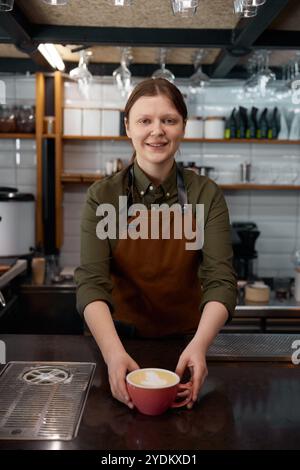 Portrait du barista au service d'un client qui donne un cappuccino ou un latte fraîchement préparé Banque D'Images