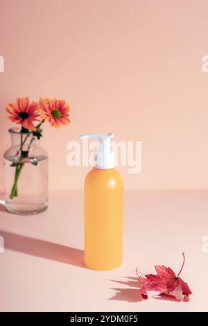 Bouteille cosmétique jaune et feuille d'automne rouge sur fond rose. Fleurs dans un vase en verre. Concept cosmétique naturel. Maquette. Banque D'Images