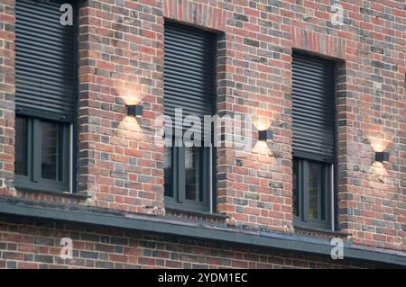 Lumière chaude éclairant les fenêtres équipées de volets de sécurité sur une façade en brique moderne, mettant en valeur le design architectural et la sécurité Banque D'Images