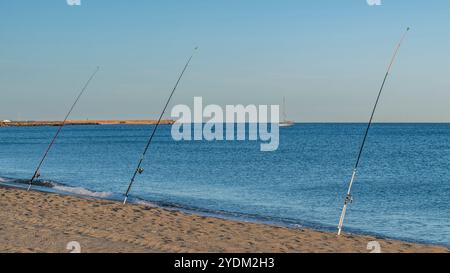 Vue panoramique de trois cannes à pêche placées sur la plage de Porto Corallo, Sardaigne, Italie, à la lumière du coucher du soleil Banque D'Images