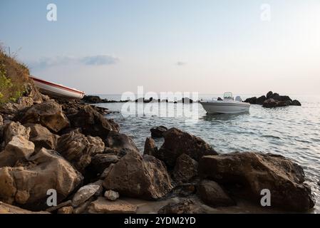 Un bateau à moteur blanc à l'ancre sur Rocky Skerry. et un bateau en bois blanc avec une bande rouge traîné dans la terre ferme. Roches au premier plan. Banque D'Images